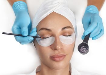 Close-up of the girl's face with closed eyes. The hand of the master tint to the eyelash with a cotton swab in cosmetology clinic.