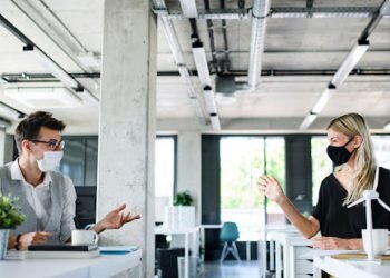 Young people with face masks back at work in office after lockdown.