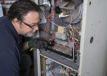 Techician looking over a gas furnace with a flashlight before cleaning it.