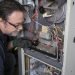 Techician looking over a gas furnace with a flashlight before cleaning it.