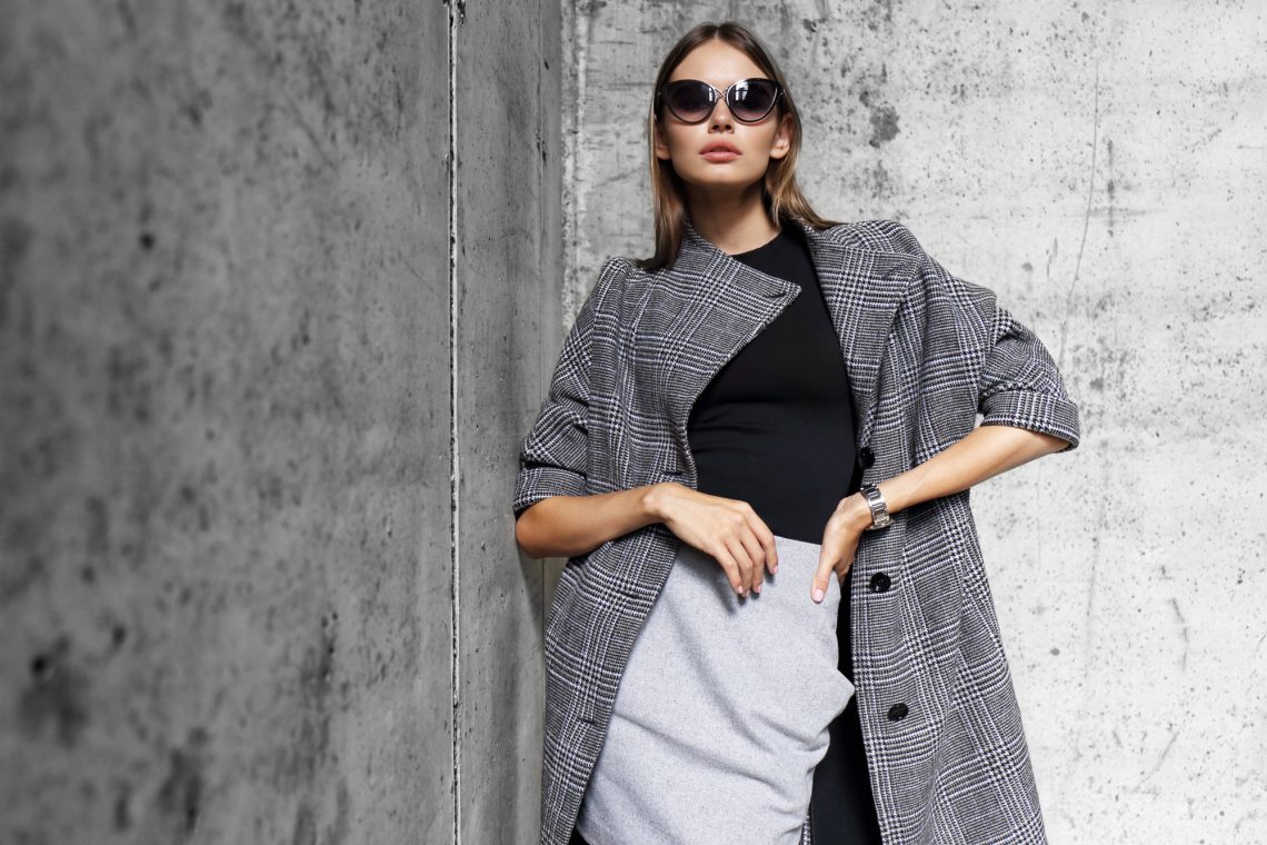 high fashion portrait of young elegant woman outdoor. Grey сoat, cat eye sunglasses, grey wall background