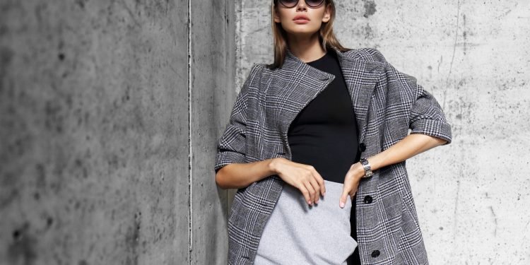high fashion portrait of young elegant woman outdoor. Grey сoat, cat eye sunglasses, grey wall background