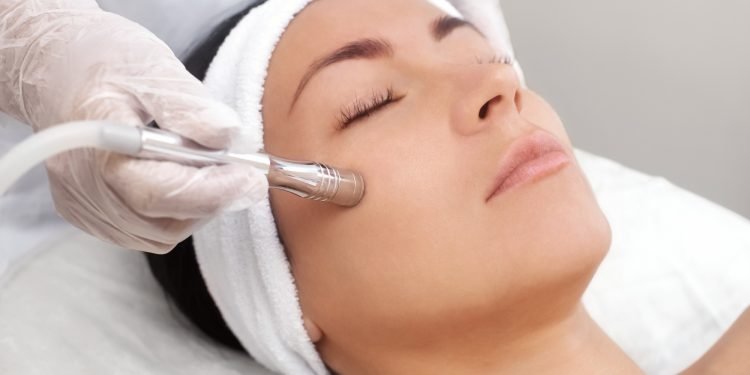 The cosmetologist makes the procedure Microdermabrasion of the facial skin of a beautiful, young woman in a beauty salon.Cosmetology and professional skin care.