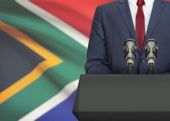 Businessman or politician making speech from behind the pulpit with national flag on background - South Africa